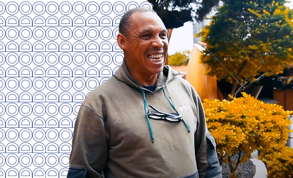 Hombre sonriendo frente a un jardín florido.